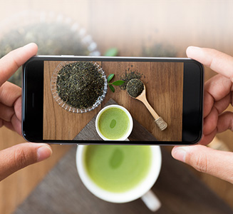 Hand hält Smartphone und fotografiert Tee